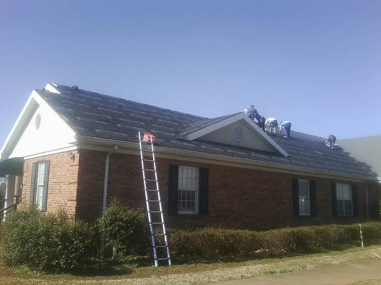 Crew tearing shingles off a brick ranch roof with a ladder set — Emergency Roof Repair work by our crew in Bushkill