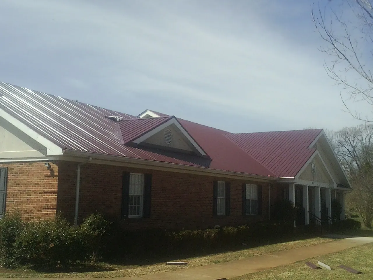 Red metal roof with gabled entries on a long brick building, from a Hail Damage Roof Repair job in Bushkill