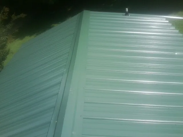 New green metal panels meeting at the ridge of a roof — Flat Roof Repair work by our crew in Bushkill