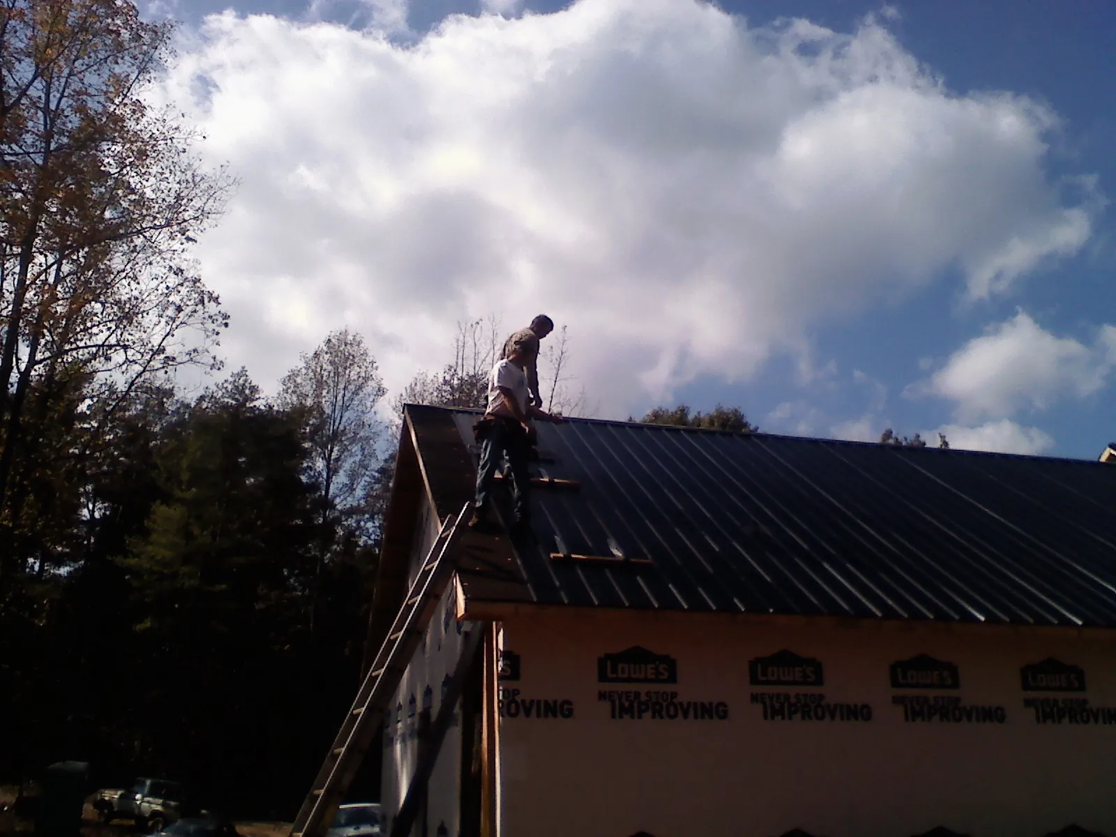 Roofer fastening dark metal panels high against a cloudy sky, from a Roof Inspection job in Bushkill
