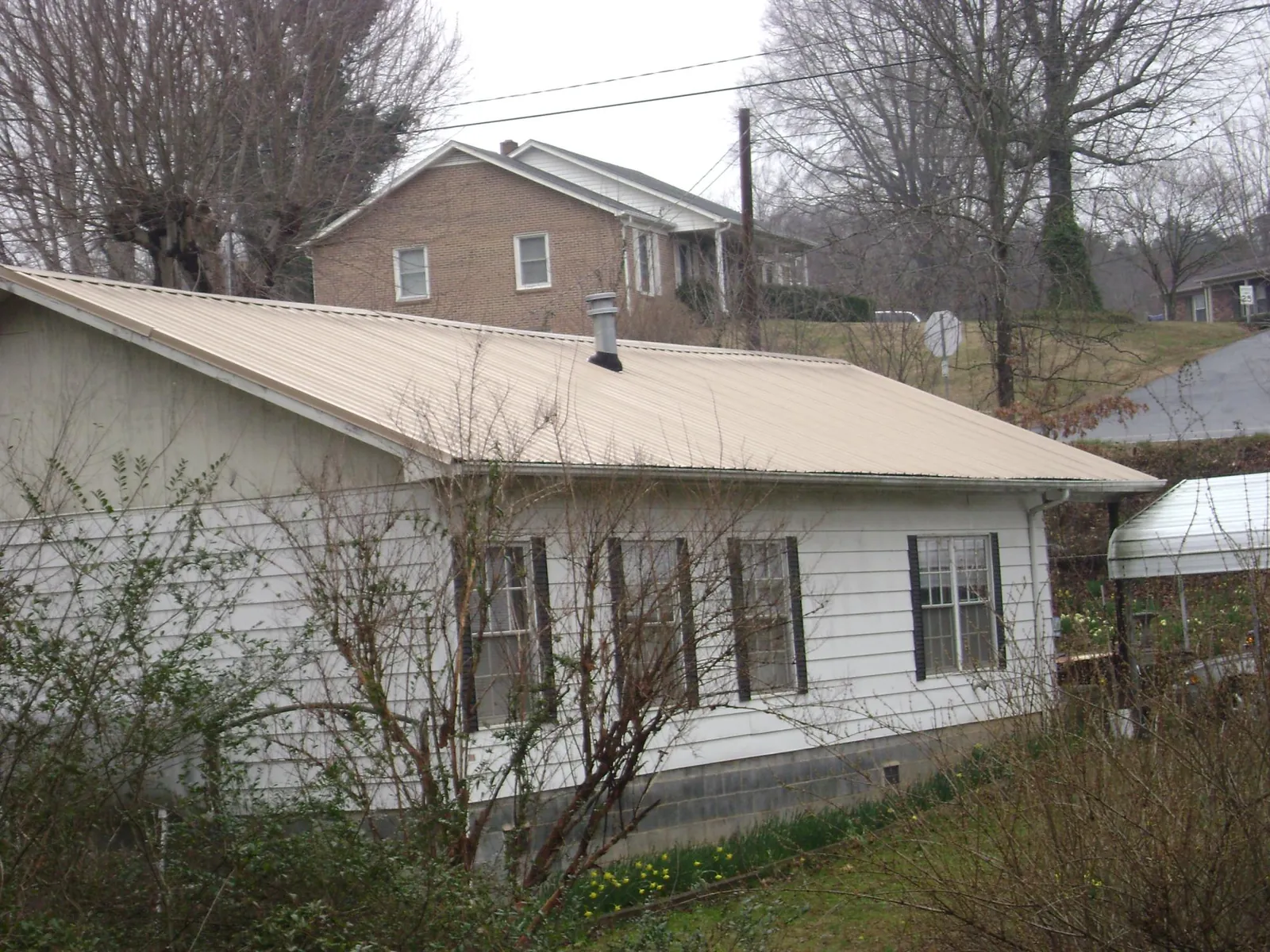 Tan metal roof on a white sided house set into a hillside — Commercial Roofing by Roofing Brothers in Bushkill